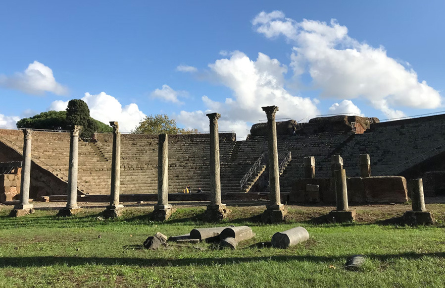 Roman theatre at Ostia Antica with tiered brick seating and a row of columns on the grass