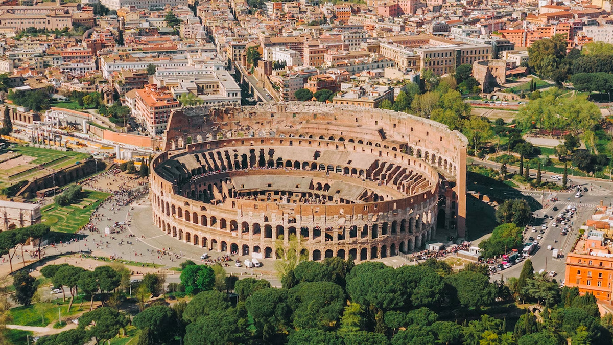 Aerial view of the Colosseum surrounded by Roman streets and green trees