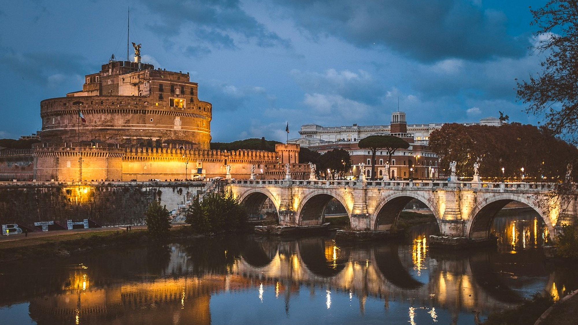 Castel Sant'Angelo and its bridge lit at dusk, reflected in the Tiber