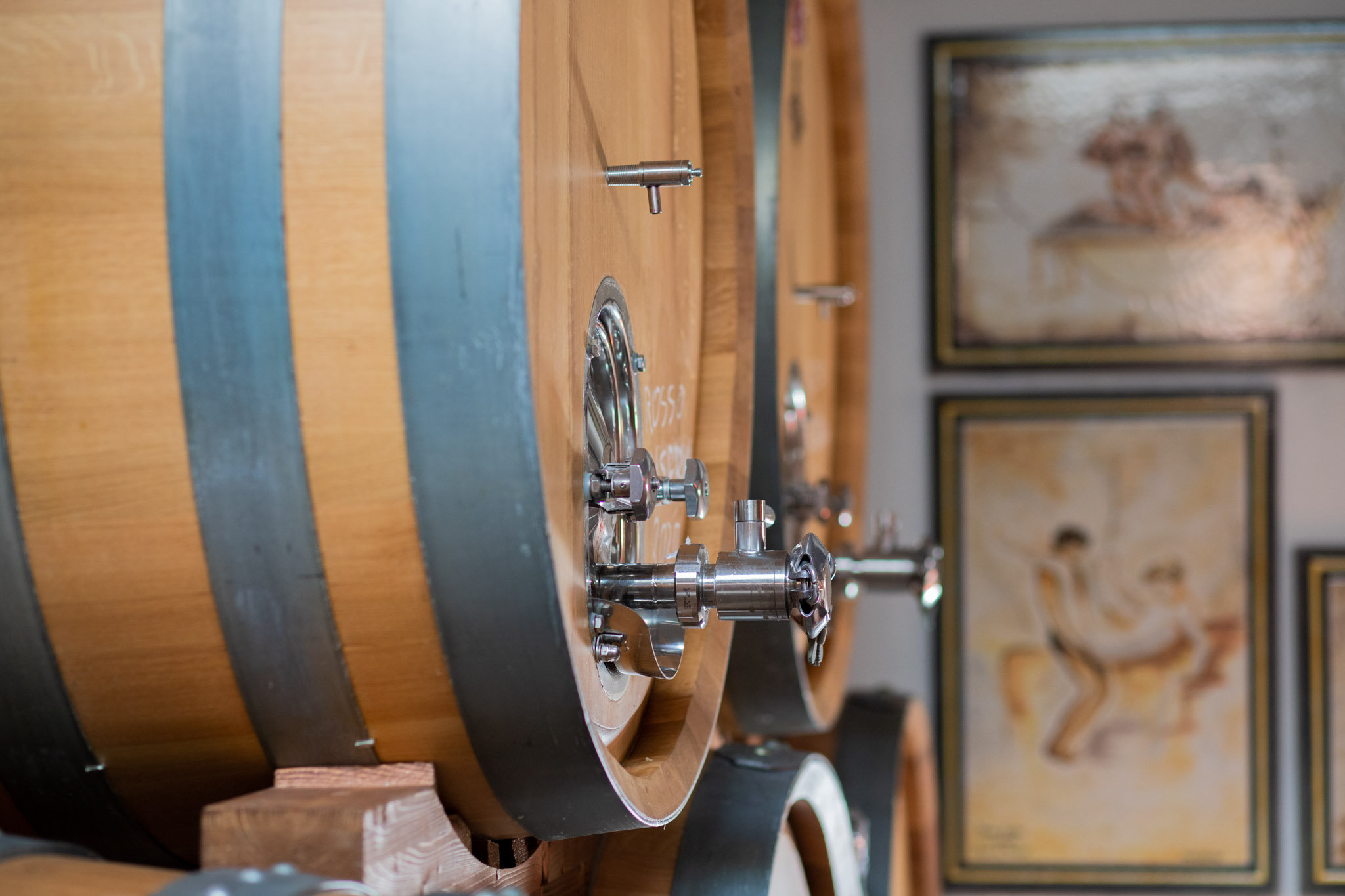 Close-up of oak wine barrels with steel taps beside framed vintage drawings