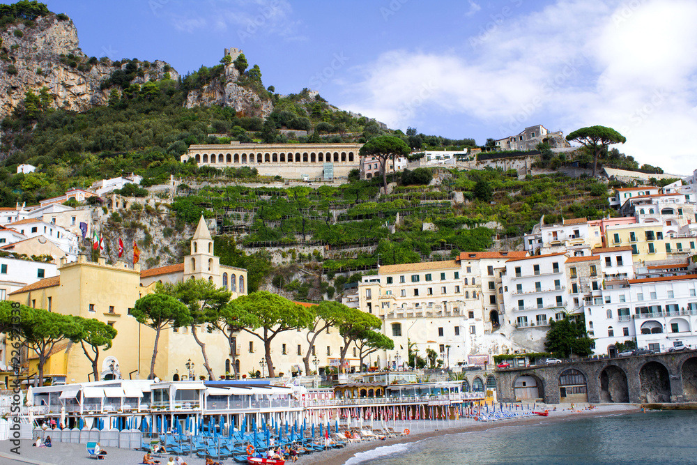 Amalfi beach with sunshades and terraced lemon groves climbing the hillside above the town