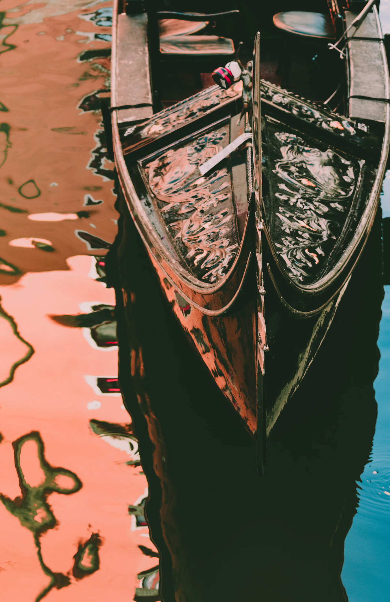 Bow of a gondola reflected in pink-tinged canal water