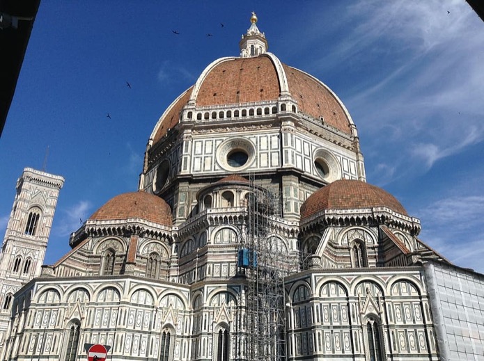 Terracotta dome and polychrome marble apse of Florence Cathedral against a blue sky, with scaffolding
