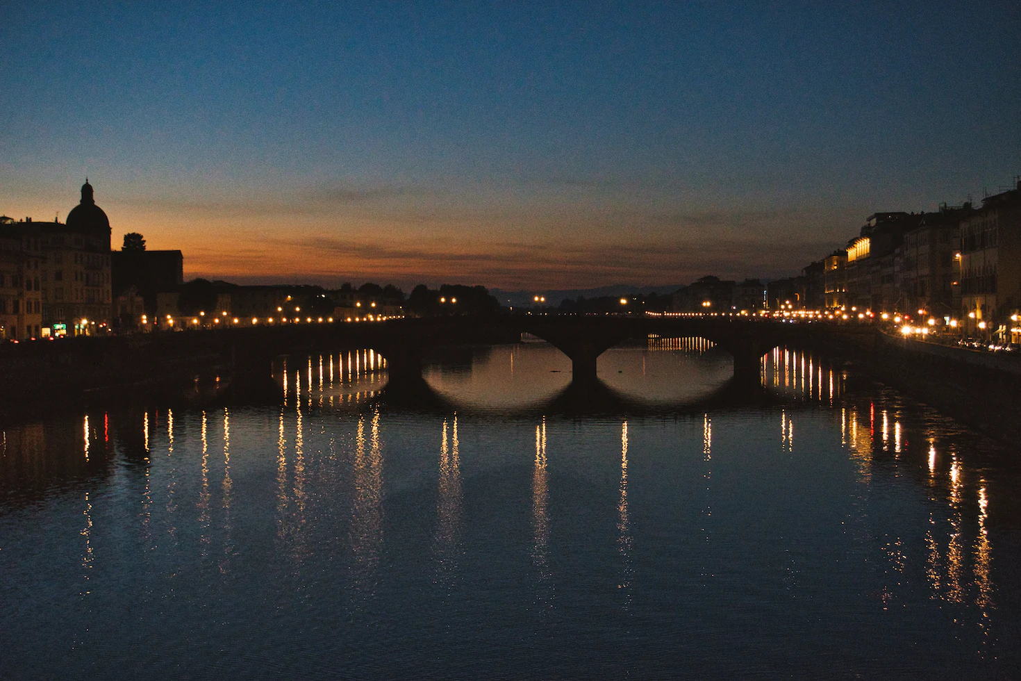 Florence's Arno river at dusk with a lit bridge reflected in the water