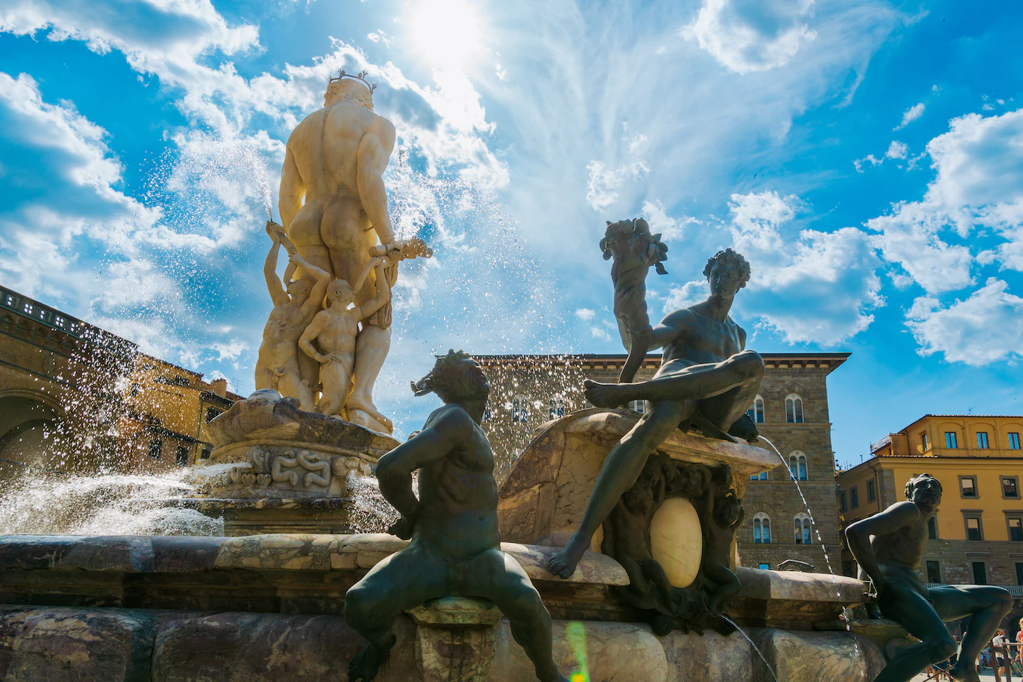 Sunlit Neptune Fountain with bronze and marble sculptures splashing against a blue sky