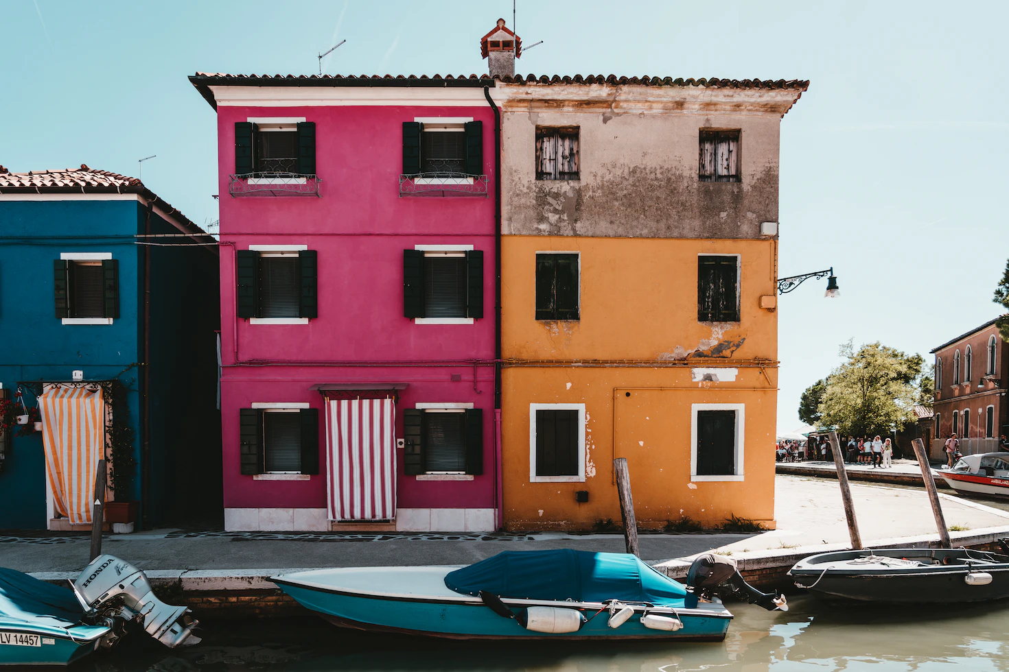 Pink and orange houses with dark shutters facing a canal, with boats moored along the edge