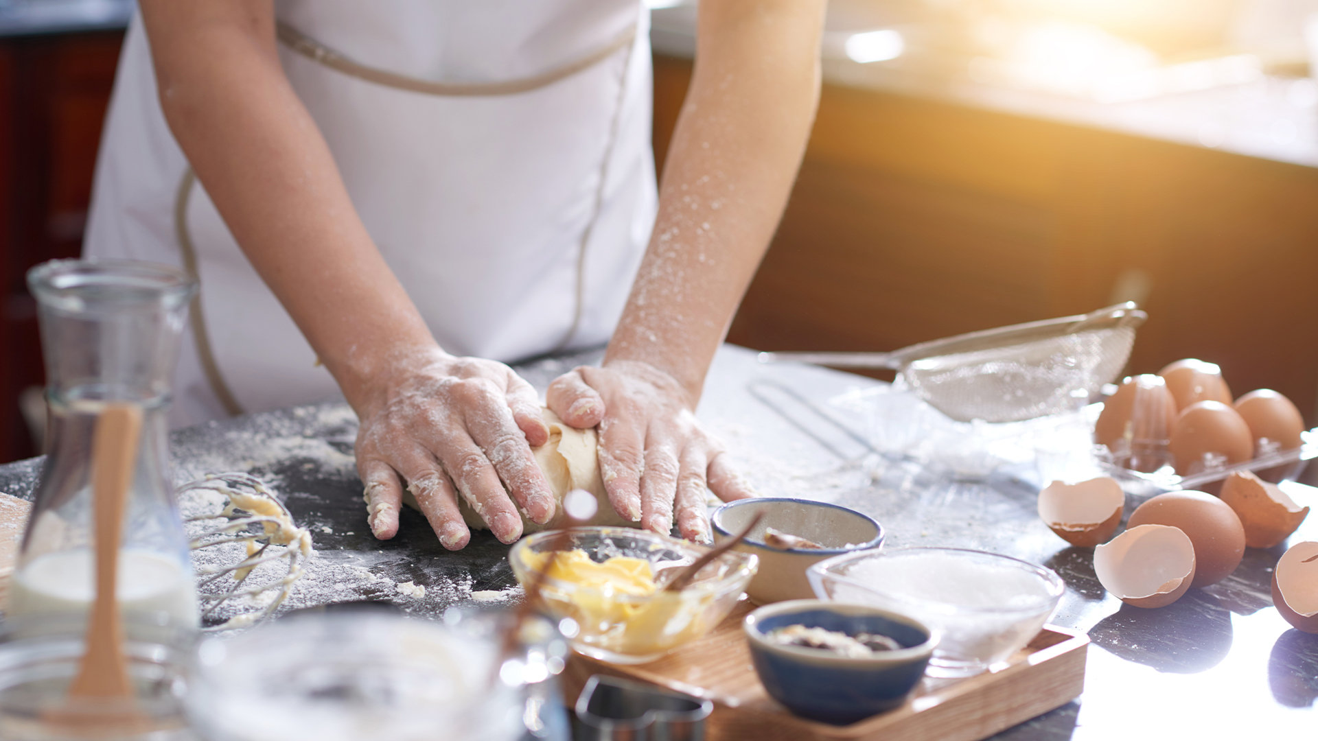 Hands kneading dough on a floured counter, surrounded by eggs and baking ingredients