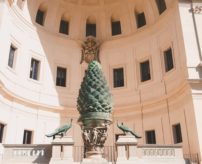Giant bronze pine cone and two peacock statues in a curved courtyard of the Vatican Museums