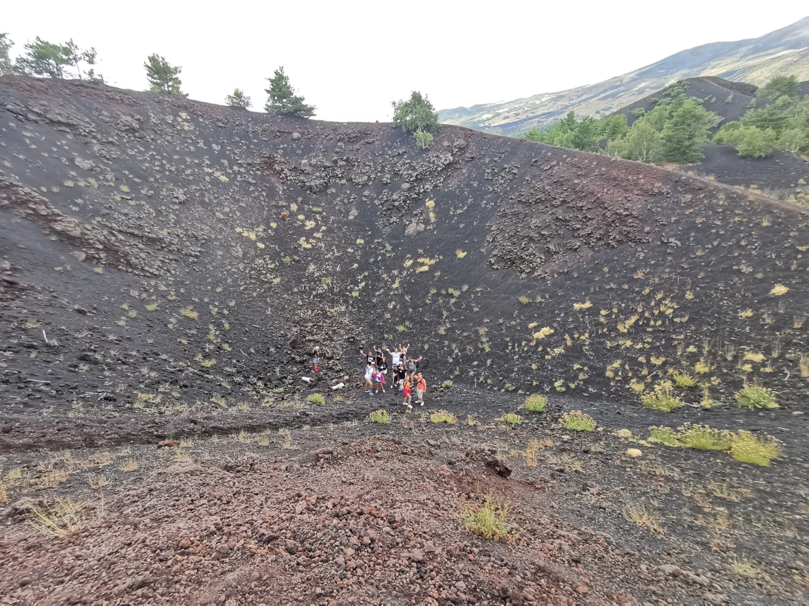 Small group standing at the bottom of an ash-covered volcanic crater dotted with grass tufts