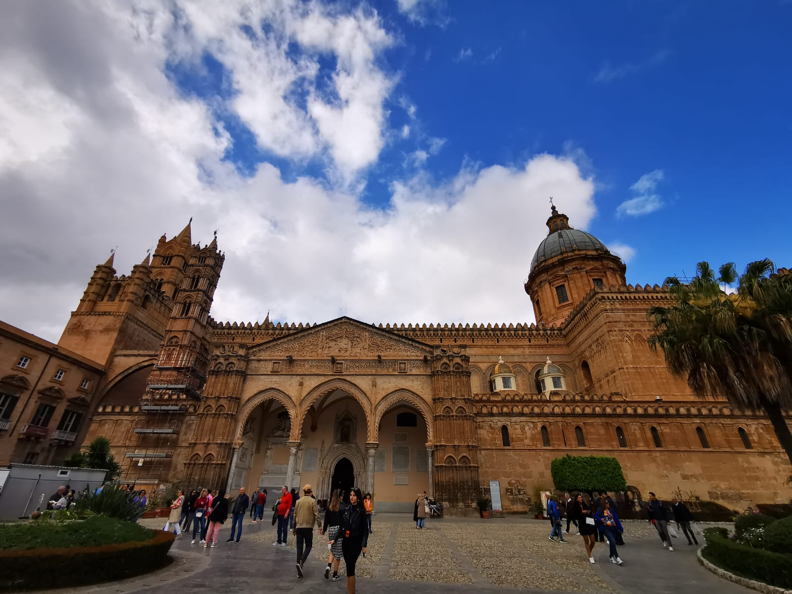 Palermo Cathedral with its Arab-Norman towers and arcaded porch under a blue sky, visitors crossing the square