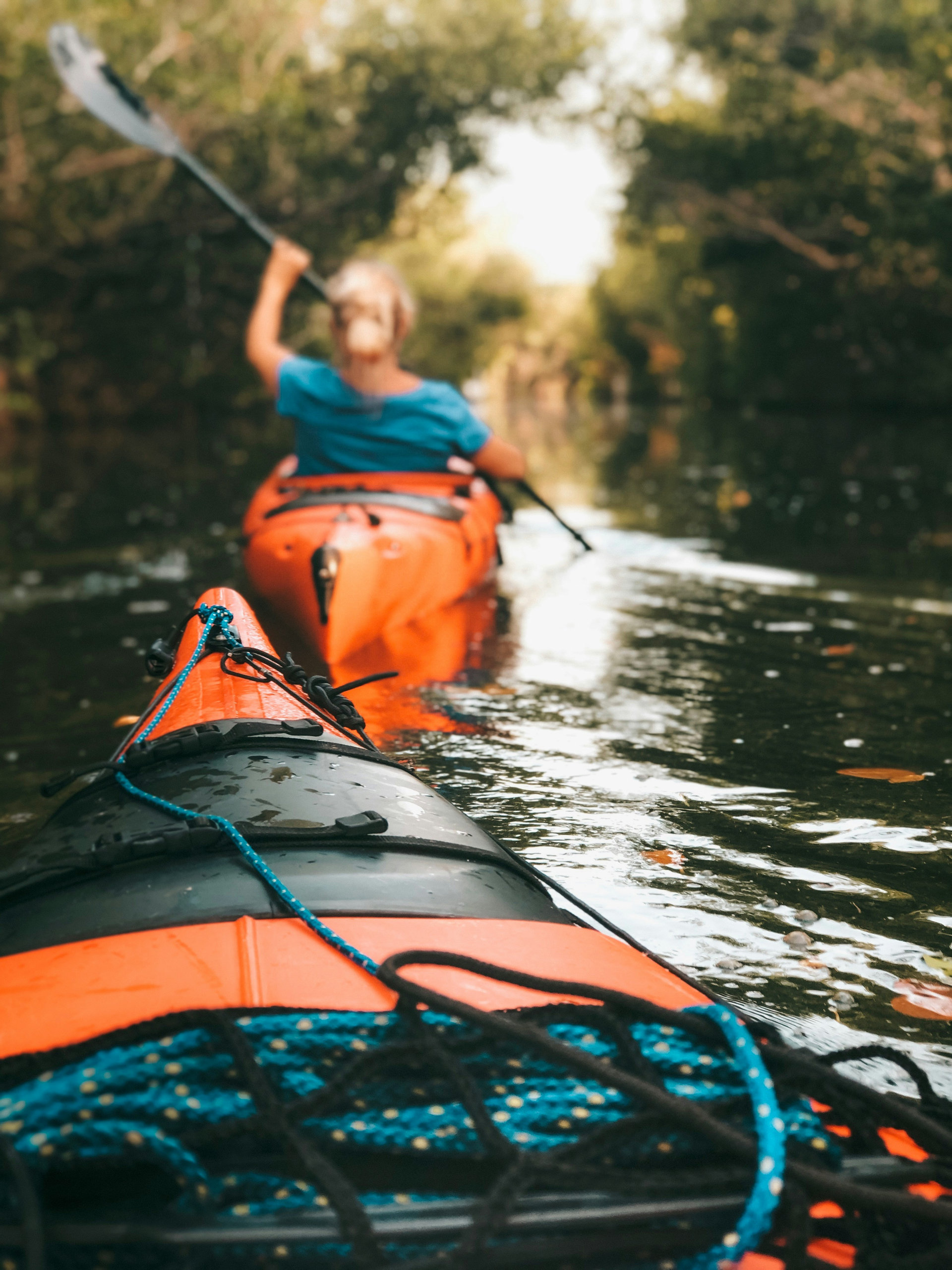 Two orange kayaks gliding along a shaded waterway lined with trees