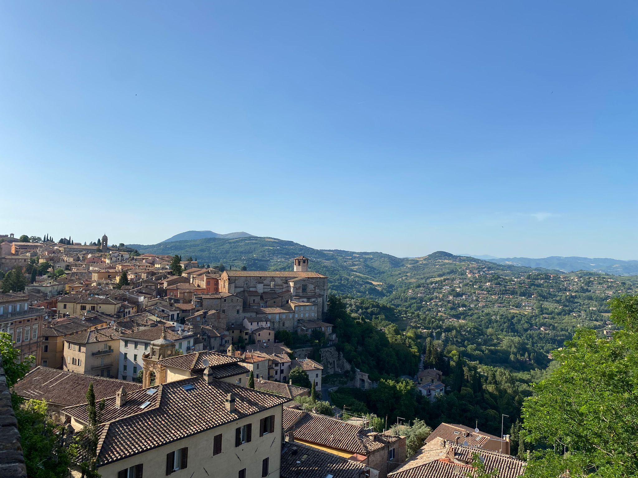 Terracotta rooftops of a hill town with green valleys and hazy hills beneath a clear blue sky