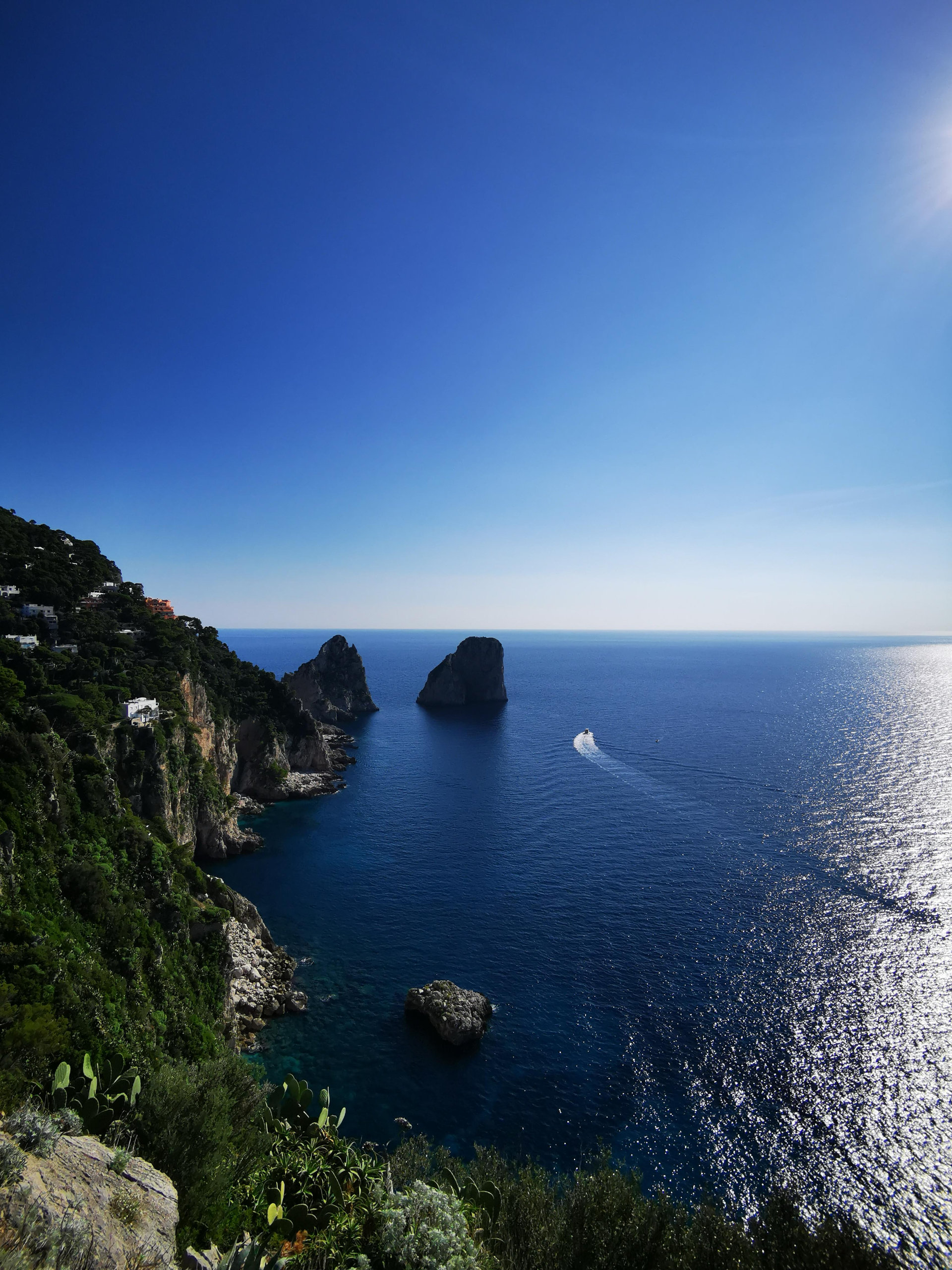 Capri's Faraglioni sea stacks rising from deep blue water, with a boat trailing white wake