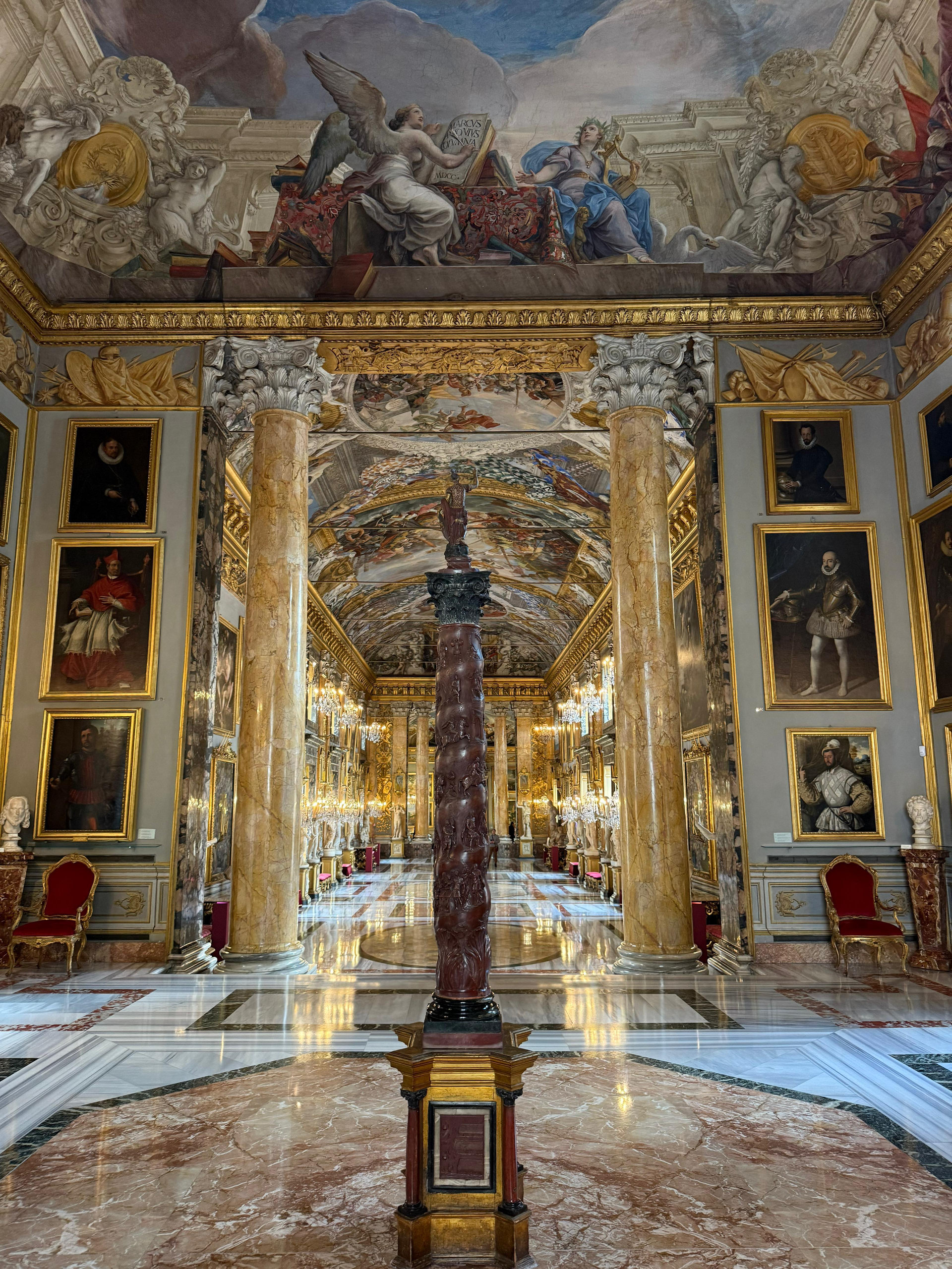 Gallery hall with a twisted red column, golden marble pillars and portraits under a frescoed ceiling