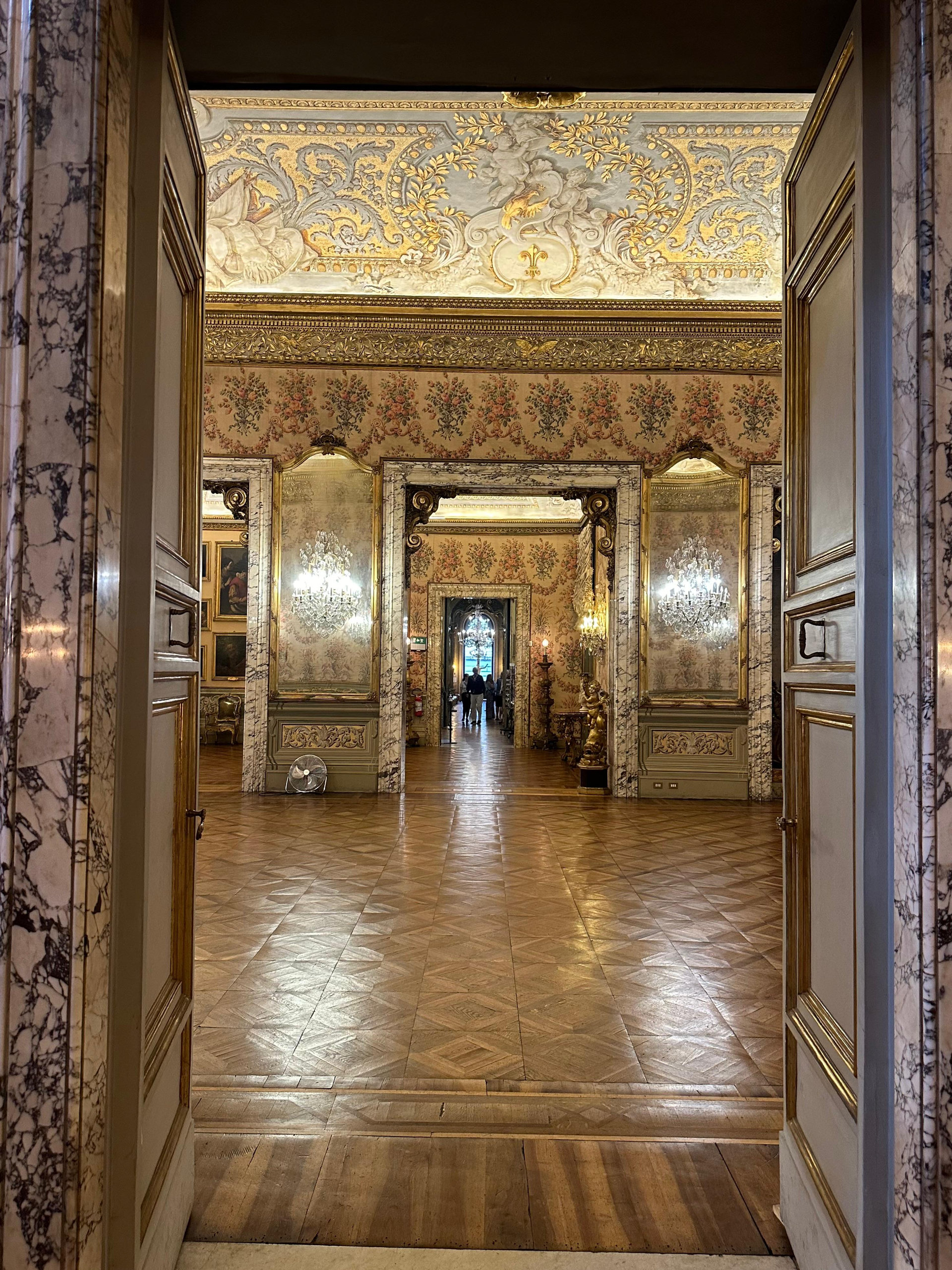 Enfilade of palace rooms seen through a doorway, with gilded ceilings and parquet floors