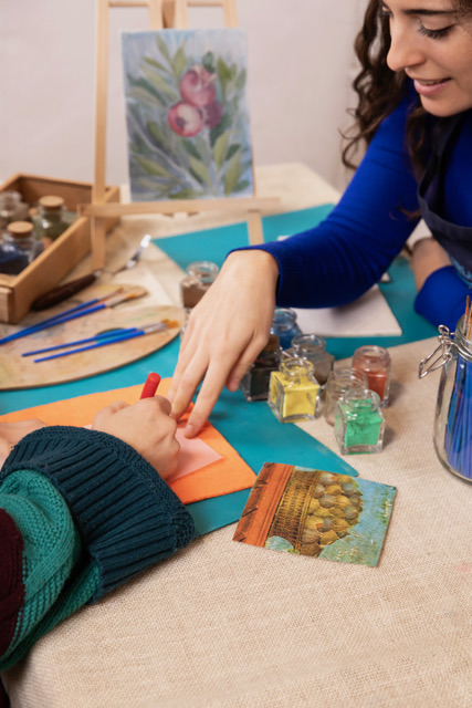 Smiling instructor pointing at a participant's work at a painting table with pots of pigment