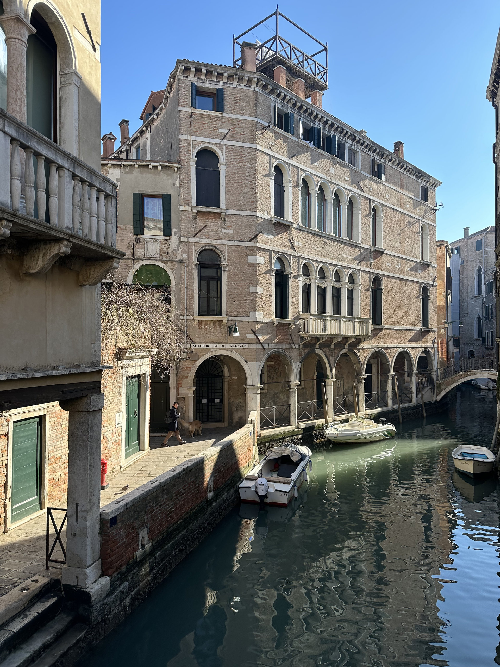 Brick palazzo with arched loggias overlooking a canal and moored boats in Venice