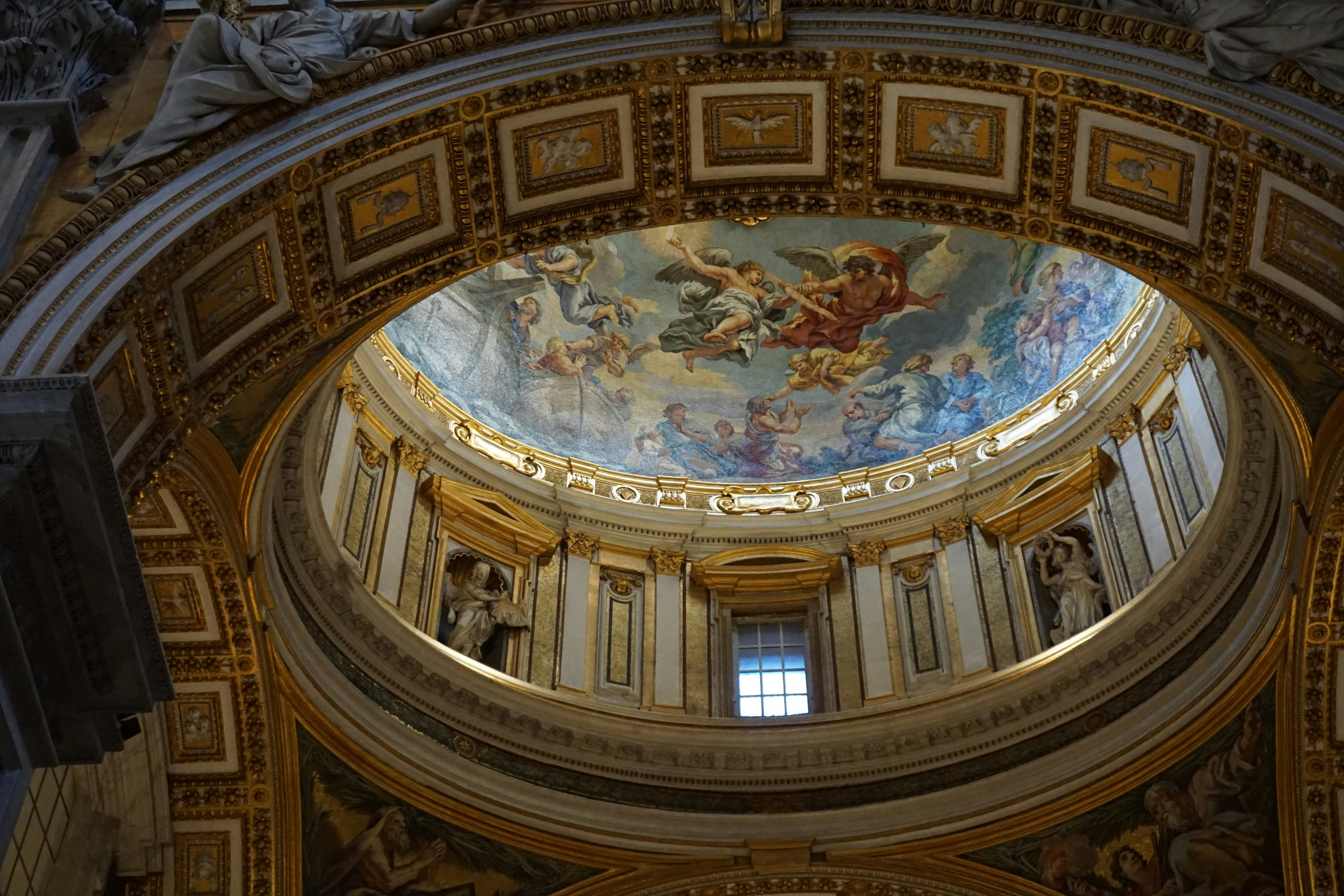 Looking up into a richly decorated dome with a painted ceiling, gilded frames and stucco reliefs