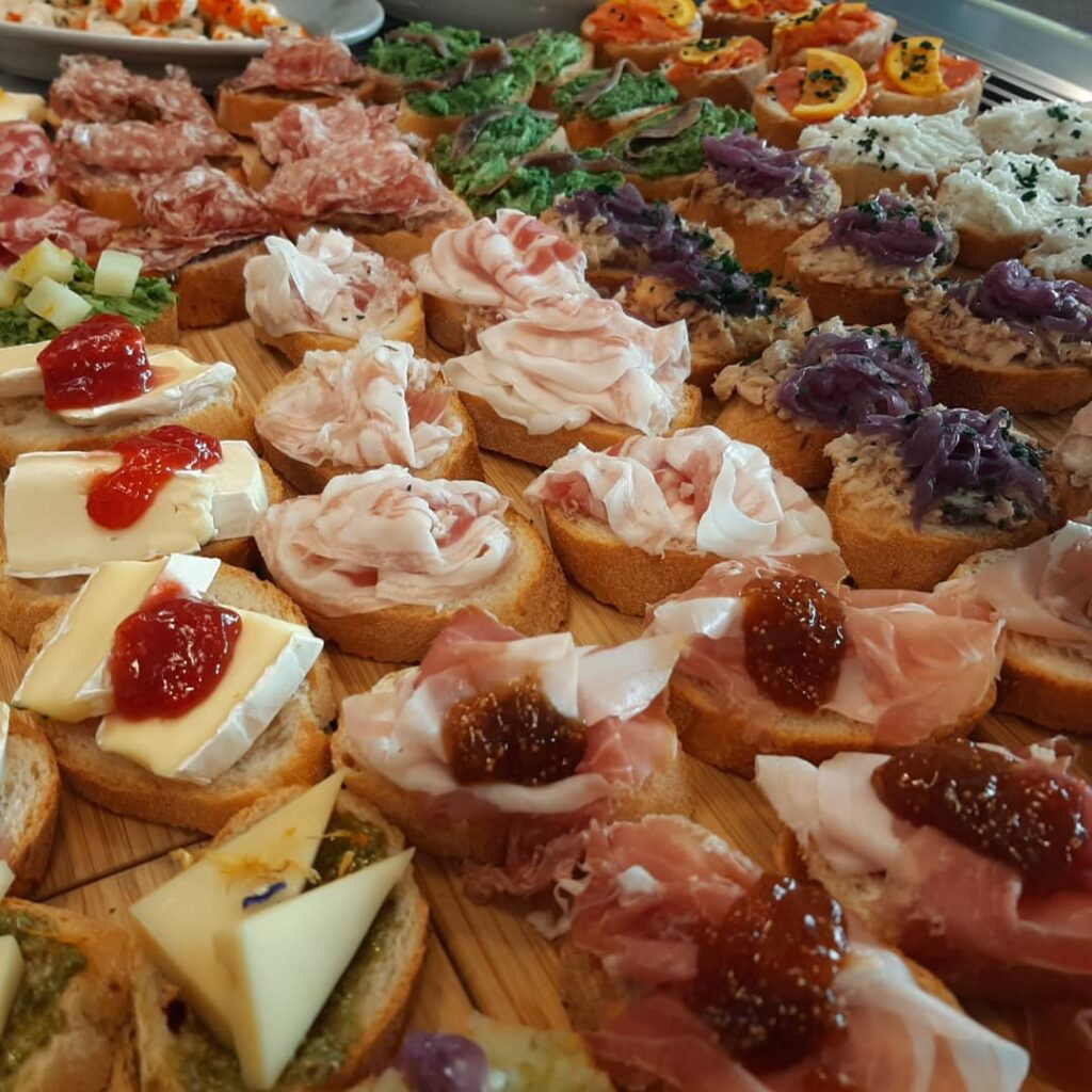 Tray of crostini topped with cured meats, soft cheeses, fig jam, pesto and vegetables