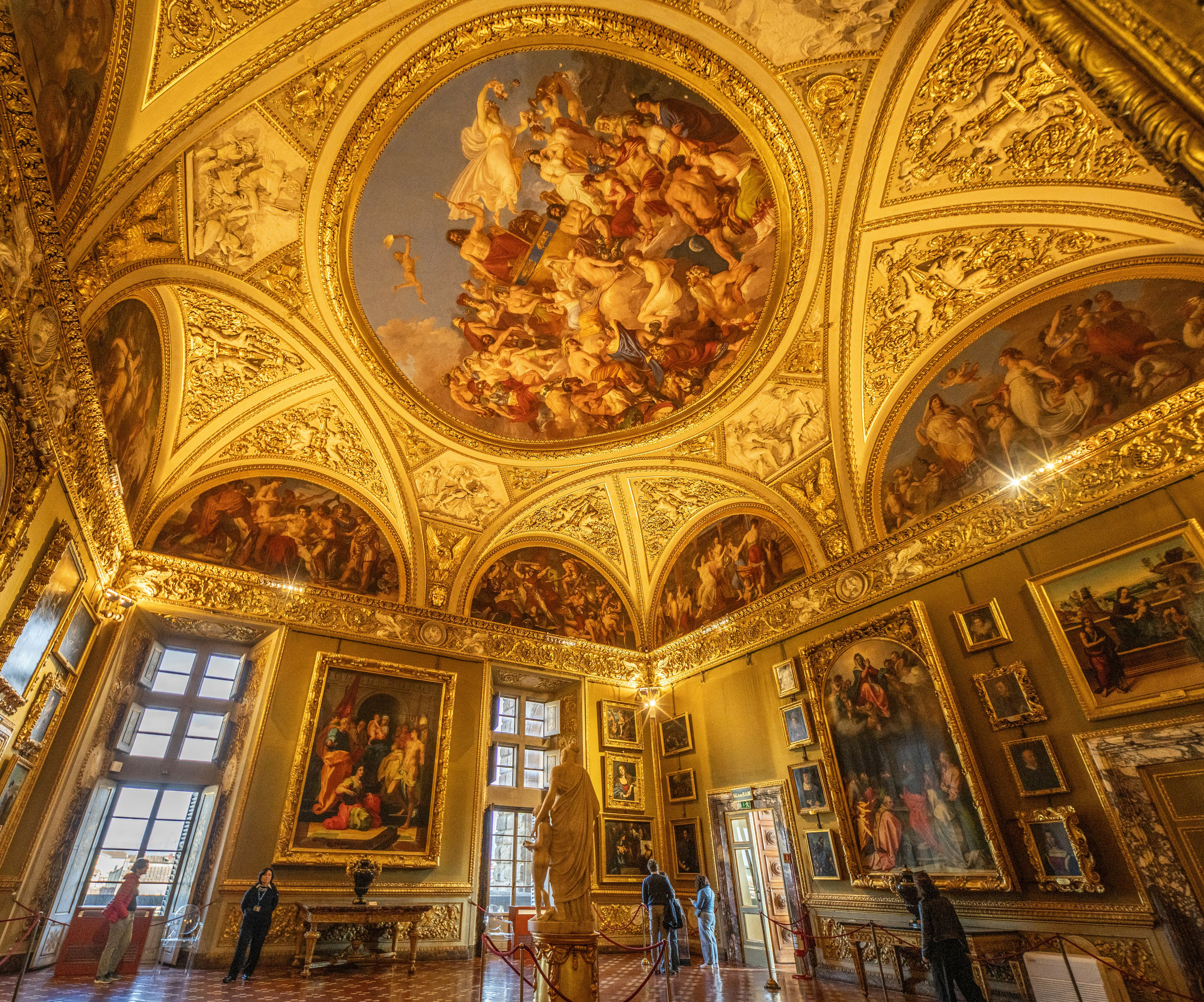 Opulent palace room with a frescoed ceiling, gilded stucco and walls covered in framed paintings
