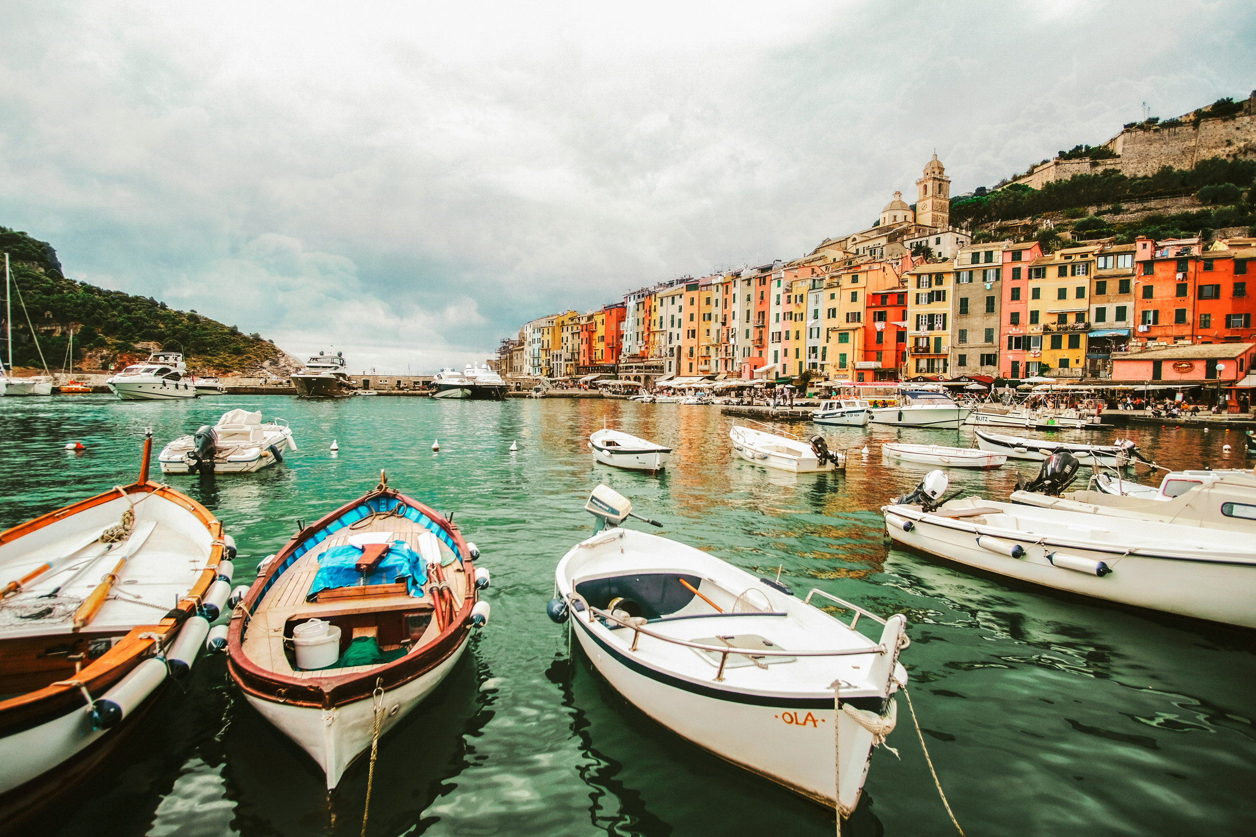 Moored boats in a harbour of green water facing a row of colourful waterfront houses
