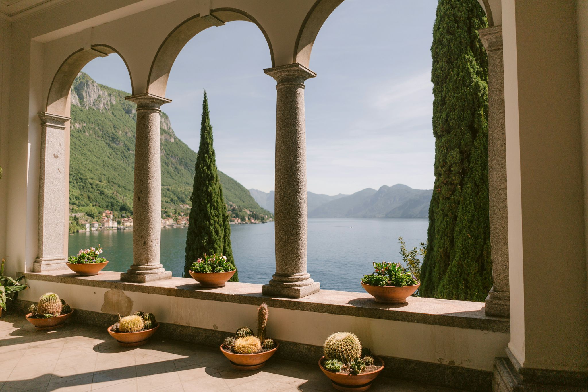 Villa loggia with granite columns and potted cacti framing cypress trees and the mountains of Lake Como